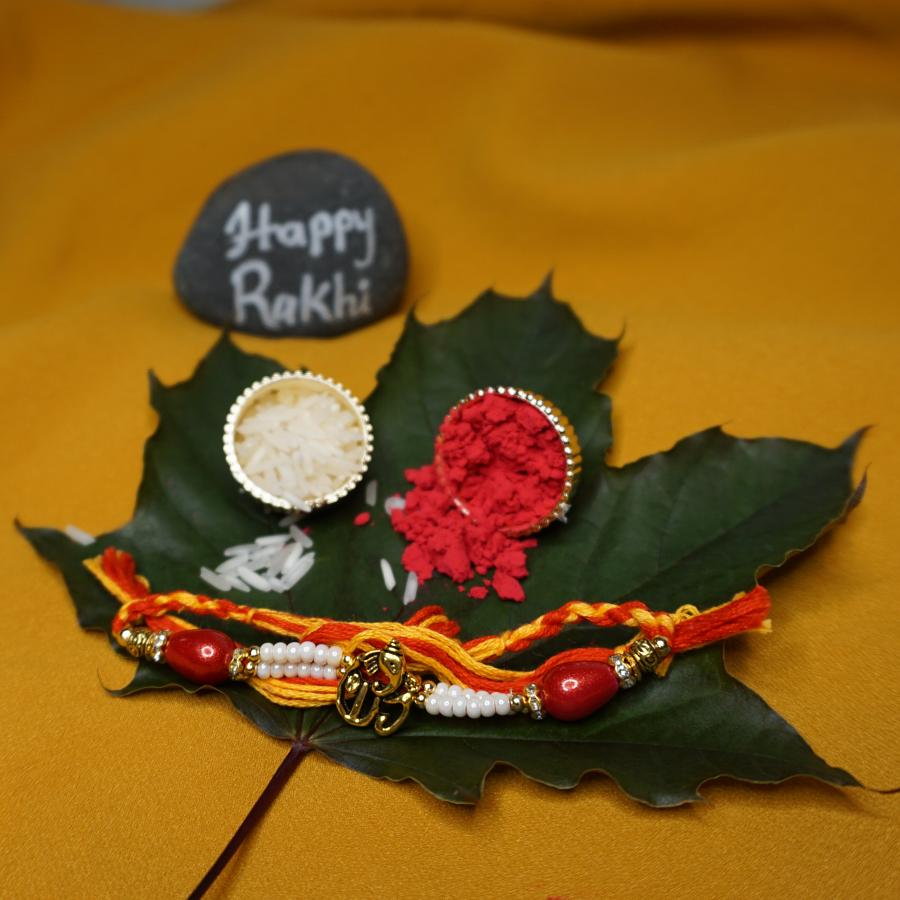 Golden Ganesh Rakhi W/ Beautiful Red and White Beads + Roli & Chaval Golden Ganesh Rakhi W/ Beautiful Red and White Beads + Roli & Chaval